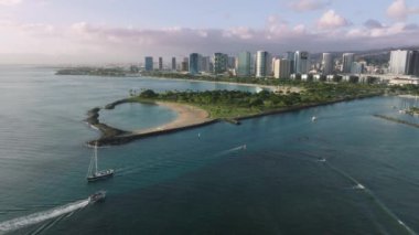 Honolulu şehir manzarası, Waikiki 'nin gökyüzü manzarası. Magic Island plaj parkında Ala Wai tekne limanı. Waikiki plajı altın gün batımı saatinde binalara yerleşiyor. Mavi okyanus yüzeyine ışık yansıyor. USA 4K