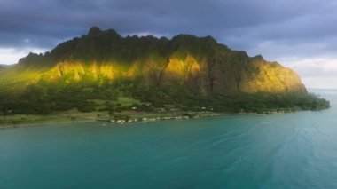 Oahu Adası 'ndaki Kualoa Çiftliği sıradağlarında gün doğumu sineması. Hawaii doğa yolculuğunun insansız hava aracı görüntüsü. Yeşil tropikal ada manzaralı dağlar altın saatinde 4K