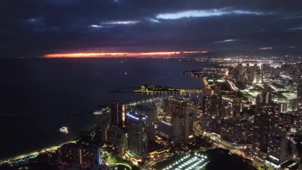 Rollドローン撮影ナイトシーン オアフ島ハワイ島のライトアップされた夜の街アメリカ ワイキキビーチリゾートの高層ビルやホテルの建物 ホノルルのダウンタウンの空中パノラマ 暗い夏の夜の光 — ストック動画