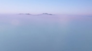 Drone, pembe gökyüzü ile gün doğumunda güzel mavi bulutların üzerinde kalın sisli bulutların üzerinde yükseliyor. İnsansız hava aracı ufuktan ufka kadar sonsuz bulut denizinin üzerinde uçuyor. İnanılmaz doğa manzarası, gökyüzünde 4K drone
