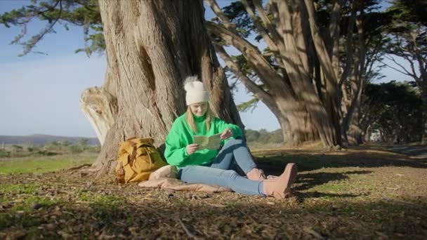 年轻的徒步旅行妇女阅读关于在森林中远足和露营探险的纸质地图 阳光明媚的早晨 女性游客在柏树下休息 呼吸着新鲜空气 背包客冒险概念 红色相机拍摄 — 图库视频影像