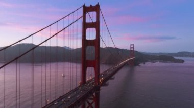 Pembe gökyüzü arka planı 4K ABD 'de gece aydınlatmalı kırmızı asma köprüsünün güzel insansız hava aracı görüntüleri. San Francisco sinematik günbatımında bir dönüm noktası. Golden Gate Köprüsü 'nün destansı alacakaranlık gökyüzü manzarası.
