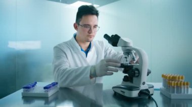 Tıbbi araştırmacı bilim adamı bilim laboratuarında biyolojik örneklere dijital mikroskop altında bakıyor. Beyaz önlüklü zeki beyaz erkek laboratuvar mühendisi aşı ve ilaç üzerinde çalışıyor.
