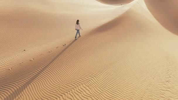 走在沙漠自然景观旁的女游客的慢动作 4K空中无人飞机拍摄的旅行妇女在金色日落时在沙丘上留下脚印的镜头 美国加利福尼亚金色沙滩上的长影 — 图库视频影像