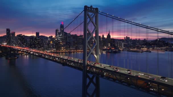 サンフランシスコのダウンタウンとの夜の交通の完全なベイブリッジのまだ空中ショットを背景に 劇的なカラフルな夕日の空の金融街の街並み カリフォルニア州サンフランシスコ Usa — ストック動画