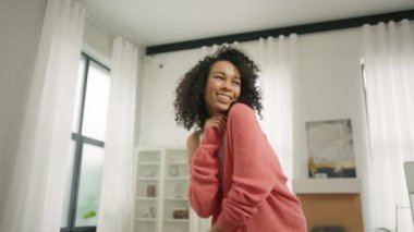 Evde dans eden kız. Güzel kıvırcık saçlı siyah genç kız ritimle hareket ediyor. Güzel bir çift ırklı dansçı kadın mutlu bir şekilde gülümsüyor. Güzel çift ırklı model özgürlüğü