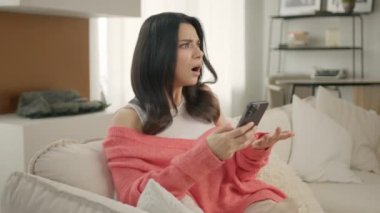 Para yüzünden sorunlarla yüzleşen bir kız. Banka dolandırıcılığı sorunu, başarısız işlem konsepti. Endiseli kadin kanepede oturmus elinde akıllı telefonuyla e-banka uygulamasini kullanarak güvensiz online ödeme yapmaya calisiyor.