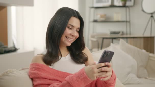 快乐他的恐慌女孩拿着手机 拉丁裔女性在家里使用智能手机装置 在社交媒体上发布年轻的拉丁女性博主的微笑 在网上购买 用4K应用程序在网上订购产品 — 图库视频影像