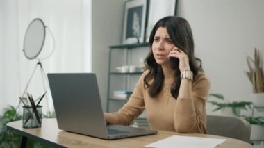 Laptop ekranına bakan hoşnutsuz genç İspanyol kadının portresi, akıllı telefon konuşması sırasında gelen kötü haberlerden memnun değil. Mobil sohbet 4K 'de kötü haber duyan mutsuz, stresli kadın kullanıcı