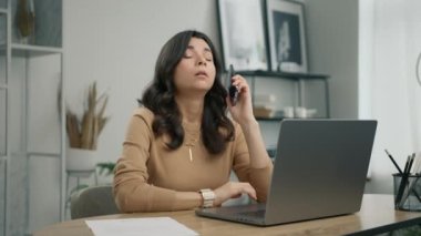 Mobil sohbet 4K 'de kötü haber duyan mutsuz, stresli kadın kullanıcı. Laptop ekranına bakan hoşnutsuz genç İspanyol kadının portresi, akıllı telefon konuşması sırasında gelen kötü haberden memnun değil.