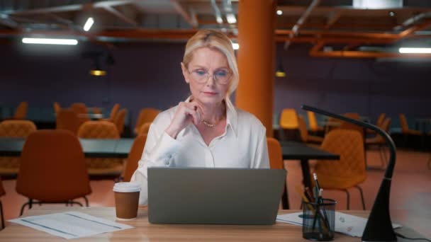 戴眼镜工作到很晚的漂亮女人 女老板在现代阁楼风格的空荡荡的办公室背景下工作 50岁的女商人在笔记本电脑上输入电子邮件 阅读4K新闻 — 图库视频影像
