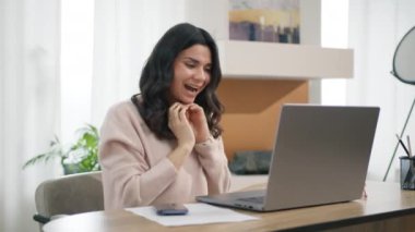 Mutlu kız online başarısını kutluyor, evdeki masaüstünde uzaktan çalışıyor. Öforik Latin bayan yeni bir iş fırsatı yakaladı. İyi haber 4K. Heyecanlı genç İspanyol kadın kazanan dizüstü bilgisayara bakıyor.