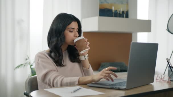在现代客厅里 西班牙裔经理一边坐在办公桌前一边 一边给咖啡饮料注入了活力 迷人的聚精会神的拉汀女人拿着杯子喝着最喜欢的咖啡 — 图库视频影像