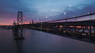 San Francisco şehir merkezindeki ufuk çizgisini ve ön plandaki Bay Köprüsü 'ndeki trafiği havadan izliyoruz. Embarcadero Limanı ve manzaralı şehir manzarası günbatımında alacakaranlıkta gökyüzünün güzel renkleri 4K USA