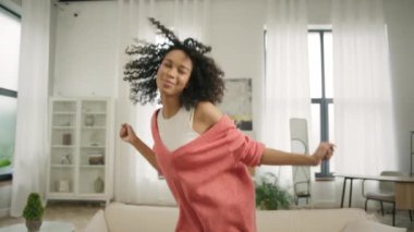 Mutluluk ve eğlence konsepti video 4K. Yavaş çekim güzel siyah kadın afro saçlı, gülümseyen ve dans eden şık modern tasarım çatı katında parlak pencereli arka planda.