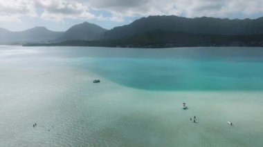 Hawaii adasında yaz tatili. İnsanlar yaz tatili boyunca Hawaii 4K 'de su sporlarından zevk alıyorlar. Arka planda açık mavi suyu ve yeşil dağları olan sinematik deniz manzarası
