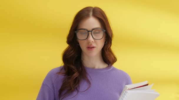ピンク色のニットセーターを着て ノートを保持し 大きなメガネでスタイルの長い髪で ふっくらした唇とかわいいブルネットの中程度のショット 黄色の背景 高品質4K映像 — ストック動画