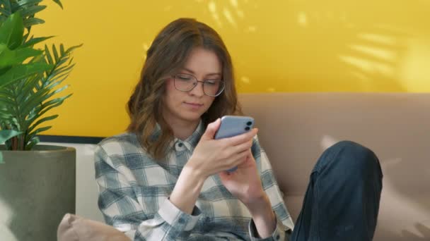 Genç Kıvırcık Saçlı Gözlüklü Bej Koltukta Oturan Akıllı Telefonlu Tatlı — Stok video