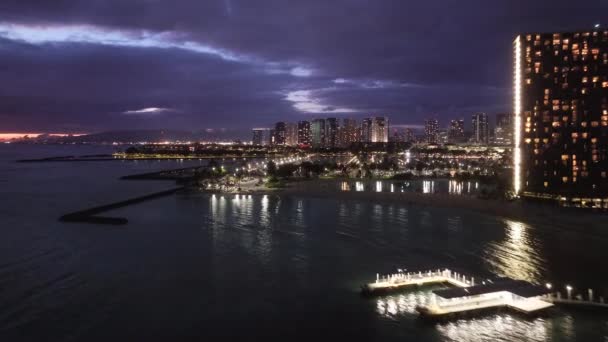 ハワイ島の街のライト4K 日没後にダウンタウンワイキキビーチ 風光明媚なホノルルスカイラインパノラマ 夜のシーンでオアフ市の空中ビュー 夕暮れ時の湾岸都市の美しい都市景観 — ストック動画