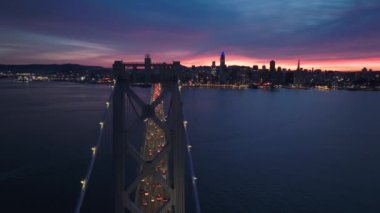 San Francisco City Skyline ve Bay Bridge 'in hava aracı destansı günbatımı ışığında. Gece körfez köprüsünden San Francisco 'ya doğru trafik vardı. Şehir merkezindeki gökdelenler uzaktaki binalar