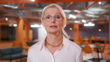 Modern ofiste kendinden emin, orta yaşlı, yaşlı, yaşlı kadın iş kadını CEO 'su kameraya konuşuyor. İş kadını yönetici konsepti. Yakın çekim vesikalık fotoğraf 4k ağır çekim