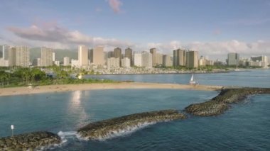 Waikiki plajı altın günbatımı saatinde binalara yerleşir ve mavi okyanus yüzeyi ABD 4K 'ya ışık yansıtır. Honolulu şehir manzarası, Waikiki 'nin gökyüzü manzarası. Sihirli ada sahil parkında Ala Wai tekne limanı