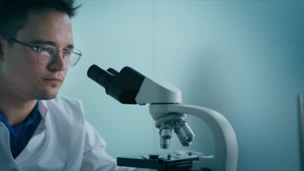 医学研究者の肖像を閉じます男性は 顕微鏡を用いた医学検査実験を行います 生物学的実験室でのサンプルを分析 プログレッシブサイエンス研究所のエンジニア — ストック動画