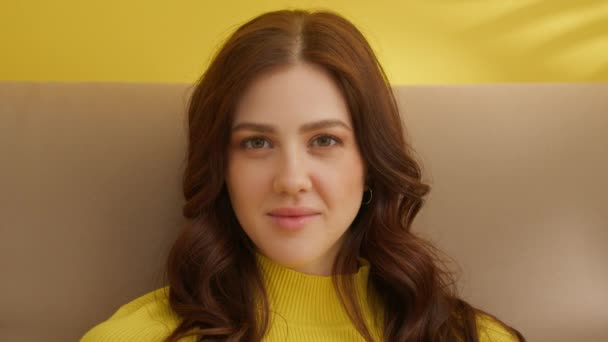 穿着黄色毛衣坐在黄色背景上的迷人的年轻黑发的画像 面容漂亮 眼睛绿 嘴唇丰满的女人 美丽的 高质量的4K镜头 — 图库视频影像