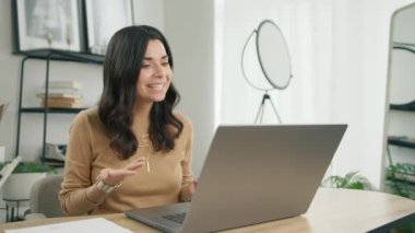 Latin kız video sohbet dili öğreniyor, ofiste oturuyor dizüstü bilgisayarı yavaş çekimde seyrediyor. Gülümseyen İspanyol kız öğrenci çevrimiçi öğretmenle e-öğrenim yapıyor, öğretmenle konferans görüşmesi yapıyor.