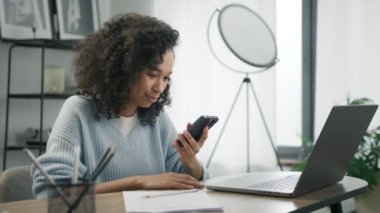 Üretken Afrikalı iş kadını bilgisayarını açıp akıllı telefon kullanıyor. Gülümseyen, enerjik, başarılı, renkli, 4K 'da çalışan bir girişimci kadın. İçişleri Bakanlığı konsepti yavaş çekimde