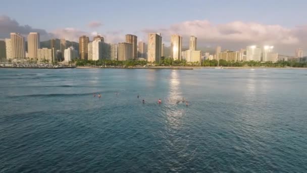 在空中看到冲浪运动员在水面上放松 等待着在现代怀基基海滩城市的运动背景下赶上海浪 火奴鲁鲁市中心上空金色落日 夏威夷4K — 图库视频影像