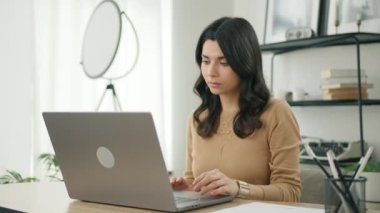 Kendine güvenen esmer bir kadının modern laptopta yazışının yan görüntüsü. Ofiste önemli e-postalar yazan Latin kadın profesyonel. Modern oturma odası uzaktan kumandalı çalışıyor