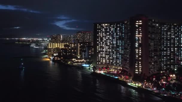 世界的に有名なホテルやリゾートに沿って ワイキキビーチで夜にドローンが飛んでいます 夕日に照らされたホノルルのスカイライン 夜のシーンで空中オアフ市 ハワイの美しい海岸線のベイシティライト — ストック動画