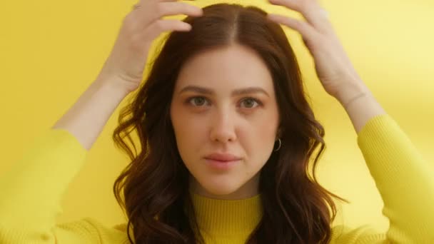 中等比例的美丽的年轻的黑头发 触摸她的手指到她的风格的头发 自信的女人穿着黄色的毛衣 看着相机 黄色背景 高质量的4K镜头 — 图库视频影像