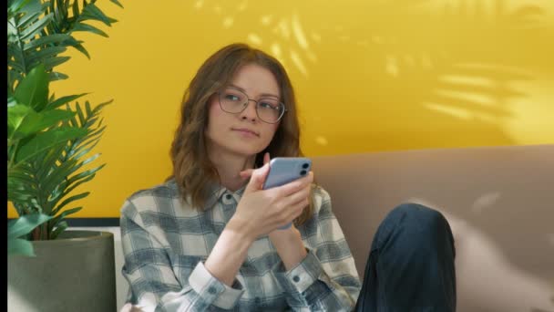 Gözlüklü Kıvırcık Saçlı Koltukta Oturan Cep Telefonu Tutan Genç Güzel — Stok video