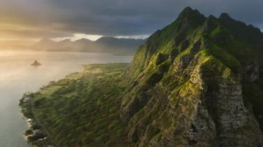 Hawaii sineması, altın gün doğumunda doğa manzarası. Volkanik dağların güzel sırtlarıyla manzaralı Oahu kıyıları. Okyanus kıyısındaki yeşil ve garip şekilli tepelerin inanılmaz manzarası. Kualoa Çiftliği 4K