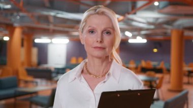 Mature blonde woman 50s successful confident strong businesswoman. Business feminism concept slow motion. Lady boss female leader woman posing looking at camera in corporate office background