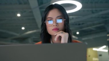 Asyalı girişimci modern gözlükler dizüstü bilgisayar 4K 'de e-posta yazıyor. Gözlüklü zeki Asyalı kadının portresini kapat. Bayan patron, bulanık arkaplan üzerine modern açık alan çatı katında proje üzerinde çalışıyor.