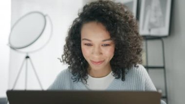 Modern şehir dairesinde cep bilgisayarı kullanan kendine güvenen Afrikalı Amerikalı kadın. Pozitif iş kızı serbest girişimci içeride otururken laptopta gülümseyen haberlere bakıyor. Başarılı bir yetişkin.
