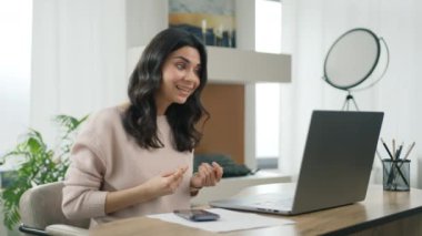 Latin kadın çalışan dizüstü bilgisayarında video görüşmesi yapıyor. Profesyonel kız el hareketlerini uzaktan izah ediyor. Gülümseyen İspanyol iş kadını yurt içi ofisinde video konferansında konuşuyor.