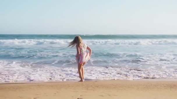 黄金の夕日の光の中で幸せなかわいい女の子のシルエット 海の波の砂のビーチでジャンプして踊る幸せな子供 子供は夢を見てる 愛らしい少女がダンサーになる夢を見る ビーチで幸せな子供 4K屋外 — ストック動画