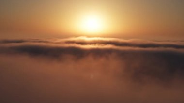 Sahne güllük gülistanlık gündoğumu. Aşağıda yüzen bulutların üzerinde parlayan büyük güneş. Gün batımındaki bulutların hava görüntüleri. Gün doğumunda hızla uçan bulutların nefes kesen hızı, 4K İHA atışı