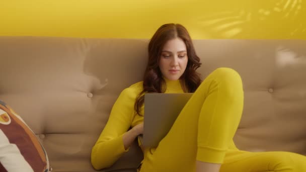Молода Красива Жінка Стилізованими Завитками Жовтому Вбранні Сидить Дивані Ноутбуком — стокове відео