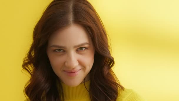 黄色の背景に黄色のセーターのキューティーの中程度のショット カメラでいちゃつく 若いブルネットの笑顔は 下を向いてカメラをまっすぐ 唇をかむ 高品質4K映像 — ストック動画