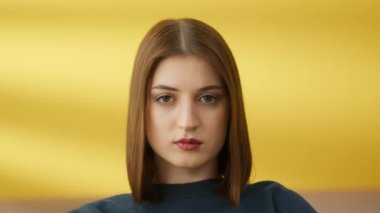 Hafif makyajlı, burnu halkalı, sarı arka planda koyu renk süveter giyen kendine güvenen genç esmer kızın portresi. Bir kadın yan yan bakıyor. Yüksek kalite 4k görüntü