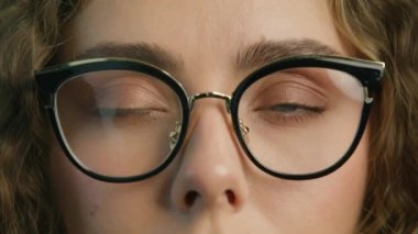 Confident woman with light green eyes and stylish eyewear, opening eyes and smiling positively 4K. Young attractive woman in black framed eyeglasses posing for close up slow motion RED camera shot