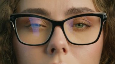 Young attractive woman in black framed eyeglasses posing for close up slow motion RED camera shot. Confident woman with light green eyes and stylish eyewear, opening eyes and smiling positively 4K