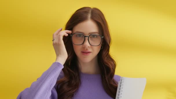 美しい若いブルネットは 魅惑的に髪に触れるノートブックで大きな光景でスタイリッシュなカールで カメラを見ています ミディアムショット 黄色の背景 高品質の4K映像 — ストック動画