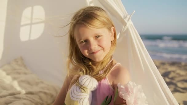 日没の太陽の光の中で幸せな女の子 美しい少女の顔を閉じてください 海のビーチでおもちゃの夢を持つ女の子 赤カメラスローモを見ている未就学児の幸せな顔 かわいい笑顔の子供の顔を閉じて — ストック動画