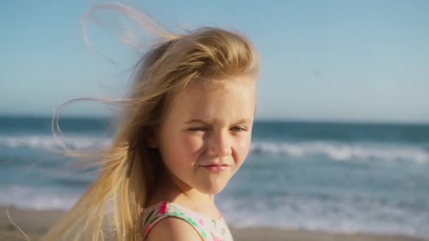 閉じるカメラを真剣に見ている少女の肖像画は 夏の夕日で海のビーチに立っている カメラを屋外で見ている思慮深い好奇心の強い子供 かわいい顔の青い目 強い顔の表情 — ストック動画